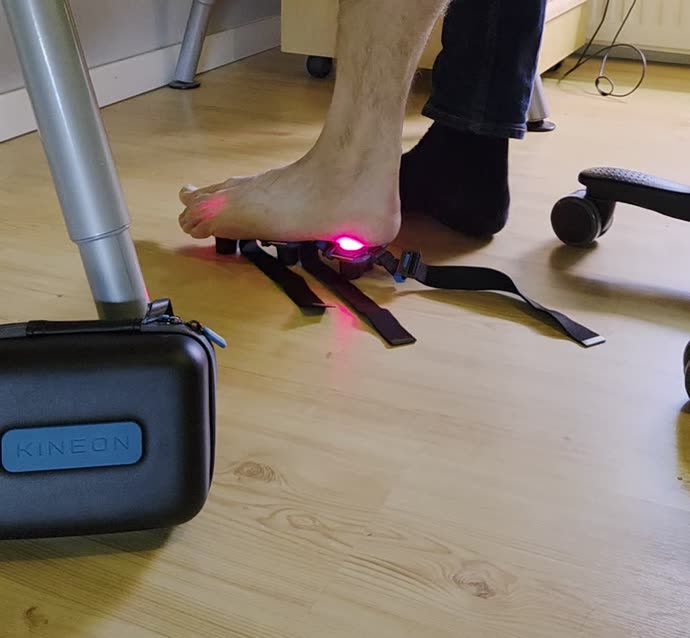 Kineon Move+ under fotsulan, rött laserljus syns lysa upp mellan tårna