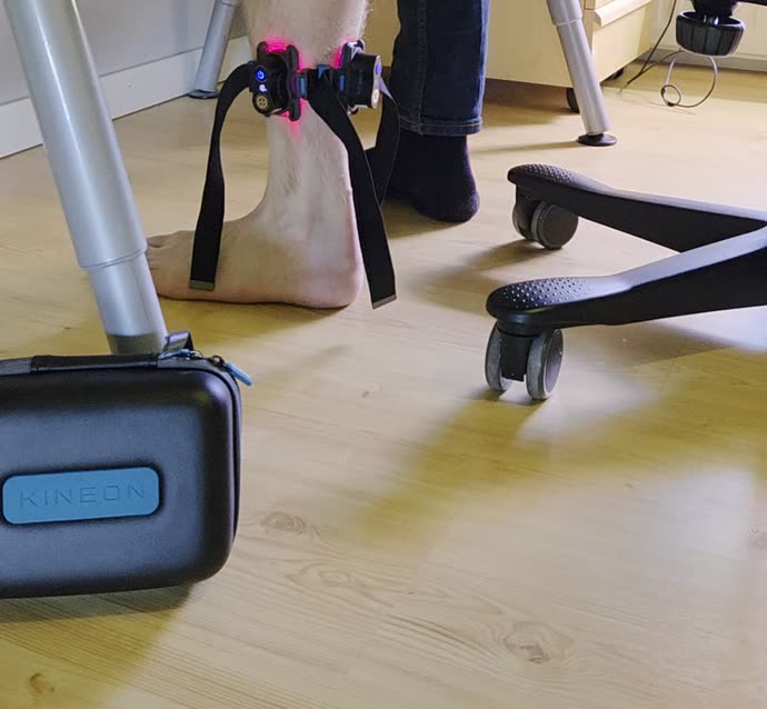 Kineon Move+ fastspänd runt vaden med rött ljus tänt, användaren sitter vid skrivbordet